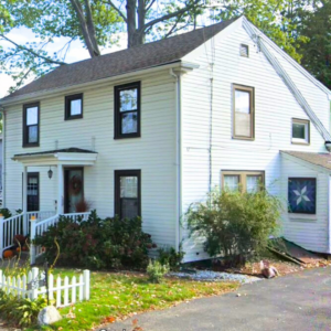 White home with black windows and worn down siding in Waltham MA