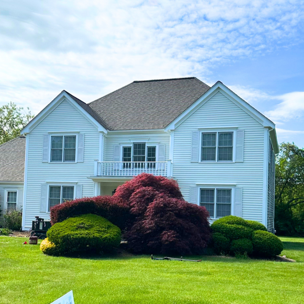 White home in Sagamore beach, MA, with lushes green grass and bushes